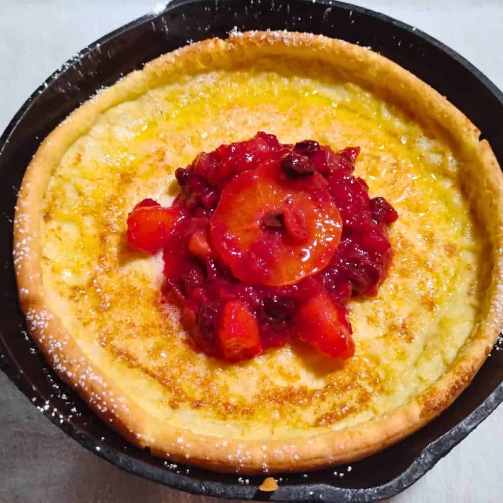 Dutch baby in a pan served with holiday cranberry orange sauce.