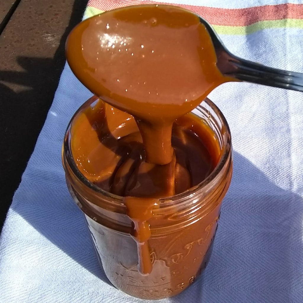 cajeta running off a spoon into a jar on a tea towel