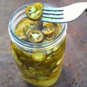 fermented jalapenos in a jar and a fork with a few slices on it.