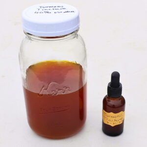 A large jar half full of turmeric tincture and a small dropper bottle filled with turmeric extract.