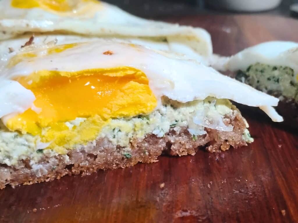 sourdough bread topped with wild greens pesto and cheese paste and topped with a fried egg.