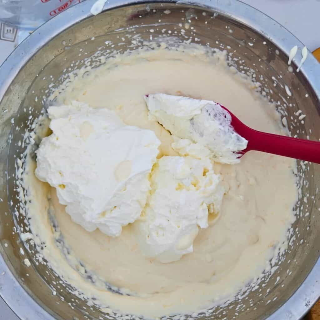 bowl full of orange quark dessert and whipped cream that is getting folded in with a rubber spatula.