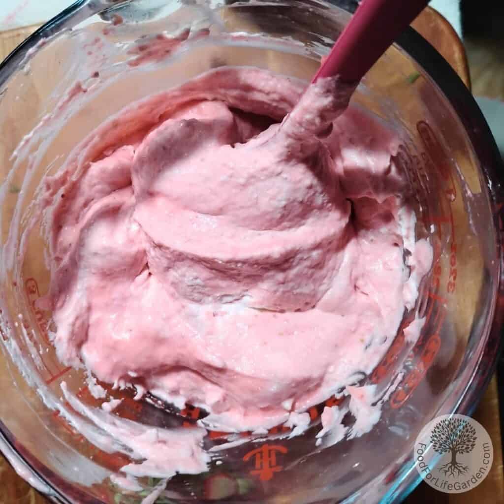 a quart size pitcher containing strawberry quark cheese mousse. Whipped cream is getting incorporated.