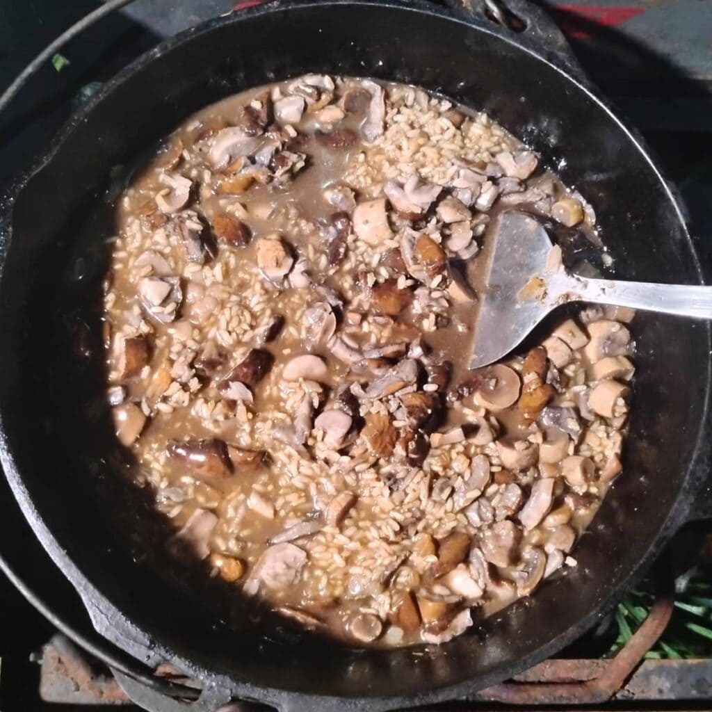 dutch oven full with mushroom risotto at the end of cooking after mushrooms and broth have been added.