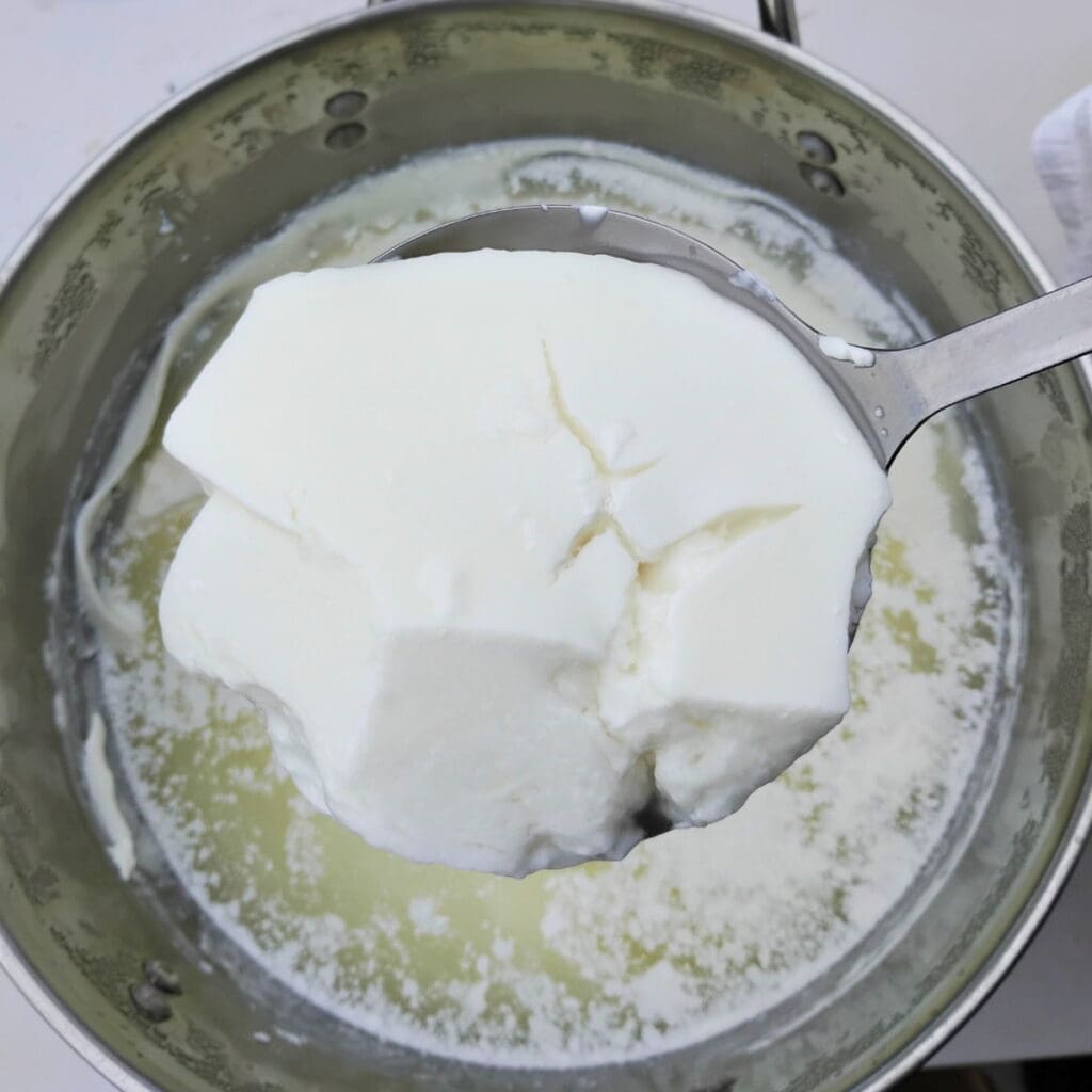 taking a skimmer full of curds from a pot to transfer to a cheese cloth
