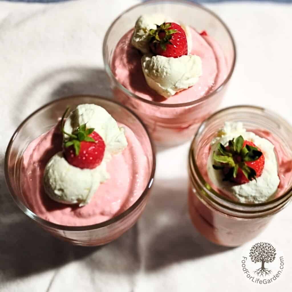 top view of three jars full of strawberry quark mousse topped with whipping cream and strawberries.