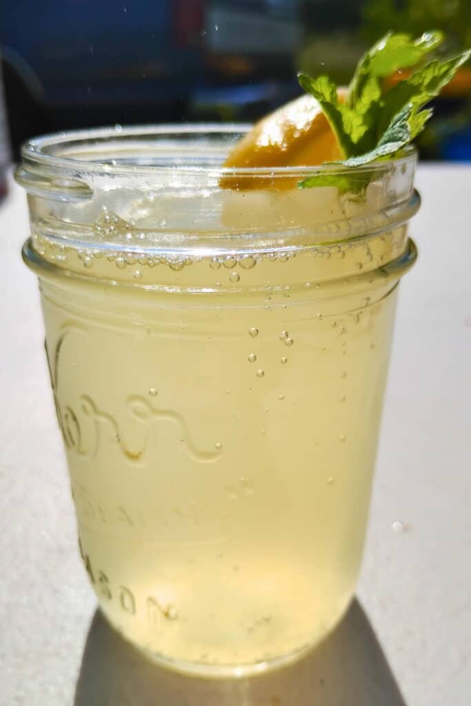 fermented lemonade in a jar with preserved lemon slice and lemon balm leaf.