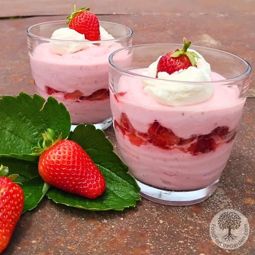 Two glasses full of strawberry quark cheese mousse with a couple of strawberries and a strawberry leave for decoration.