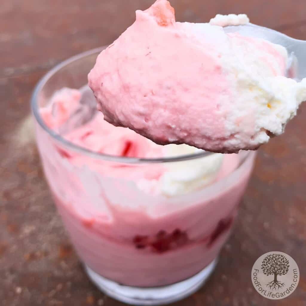A spoon with strawberry quark cheese mousse, taken out of a serving glass below.