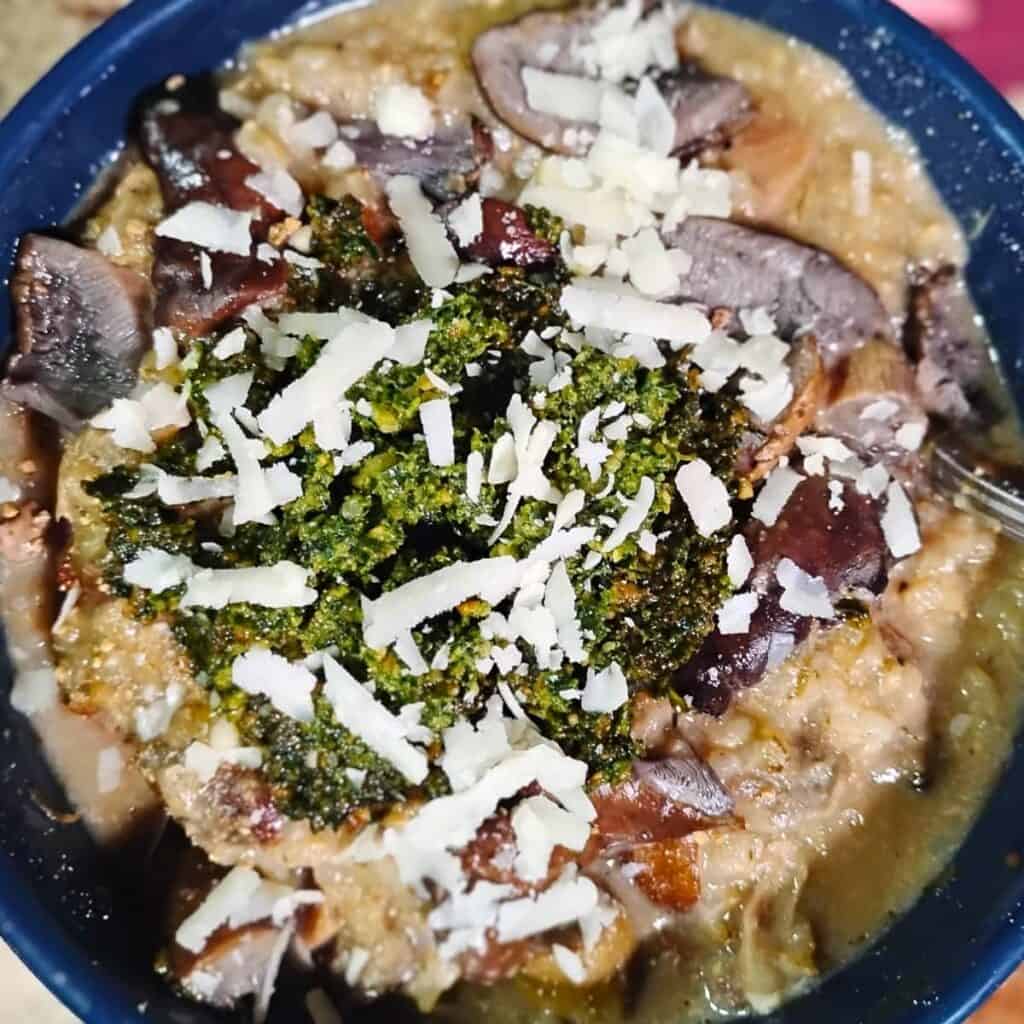 bowl full of finished mushroom risotto topped with wild greens pesto and grated cheese.