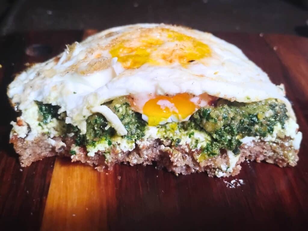 a piece of sourdough bread, topped with clabber cheese, pesto and a fried egg.