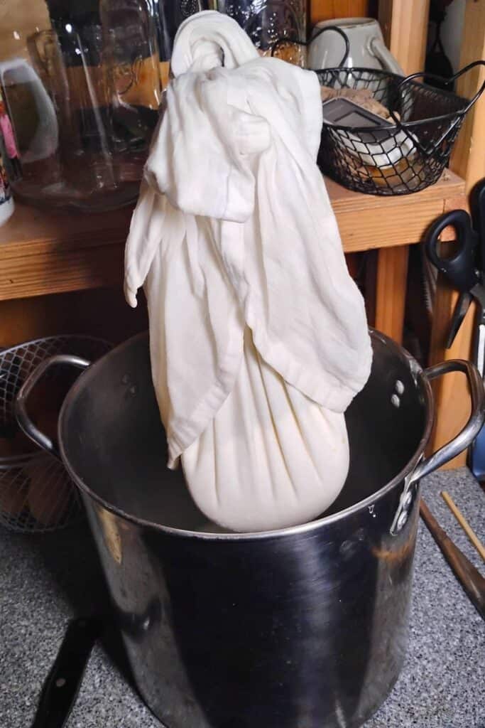 quark cheese curds are all drained inside a bag that's hanging from a hook over a pot, ready to get emptied.