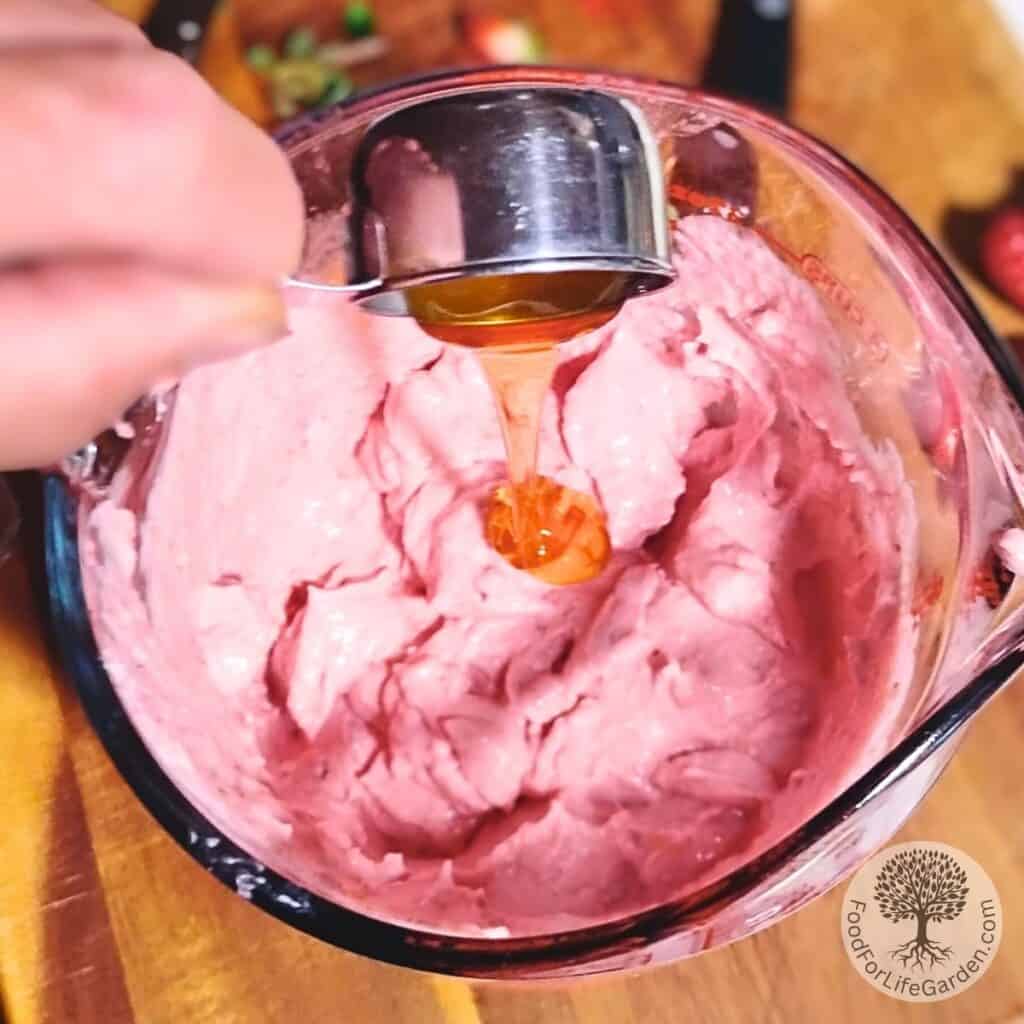 a hand is pouring honey from a measuring cup into the strawberry quark cheese cream.