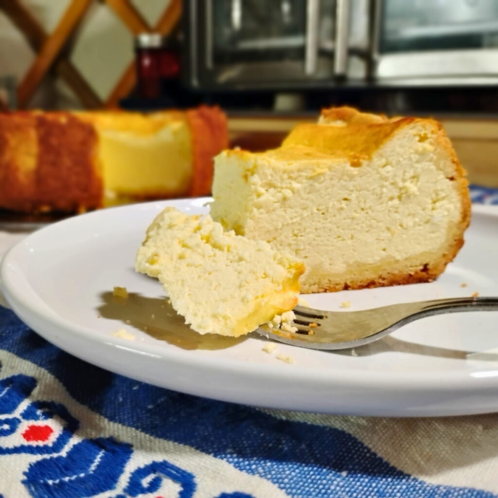 photo of a slice of German cheese cake or käsekuchen. there is a fork in the foreground that has a piece on it.