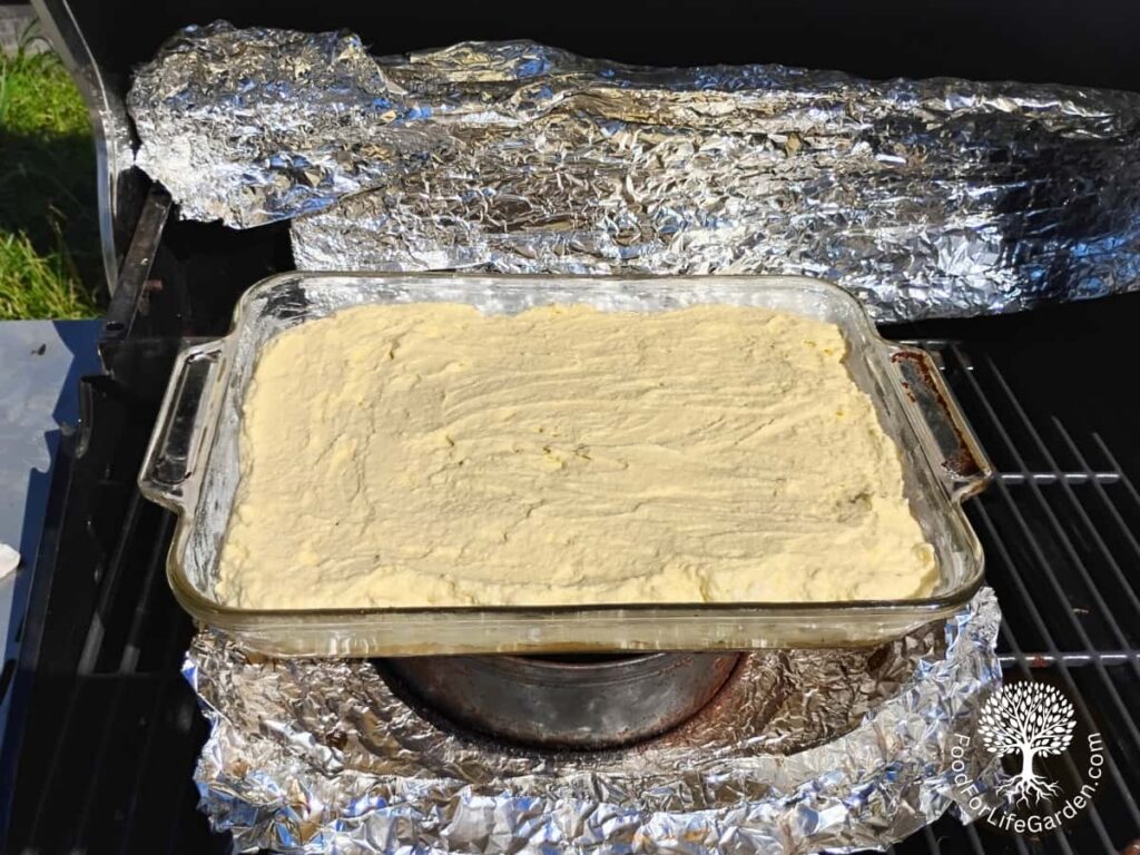 casserole dish in a BBQ grill full of cheesecake, ready for baking.