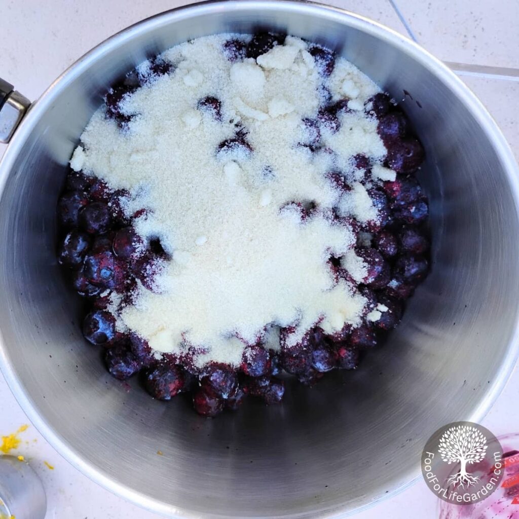 sugar and cornstarche is added to blueberries in a pot for cooking.