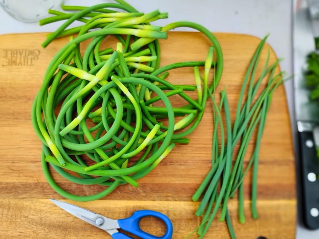 garlic scapes on a cutting board with the flower spikes cut off, laying besides them .