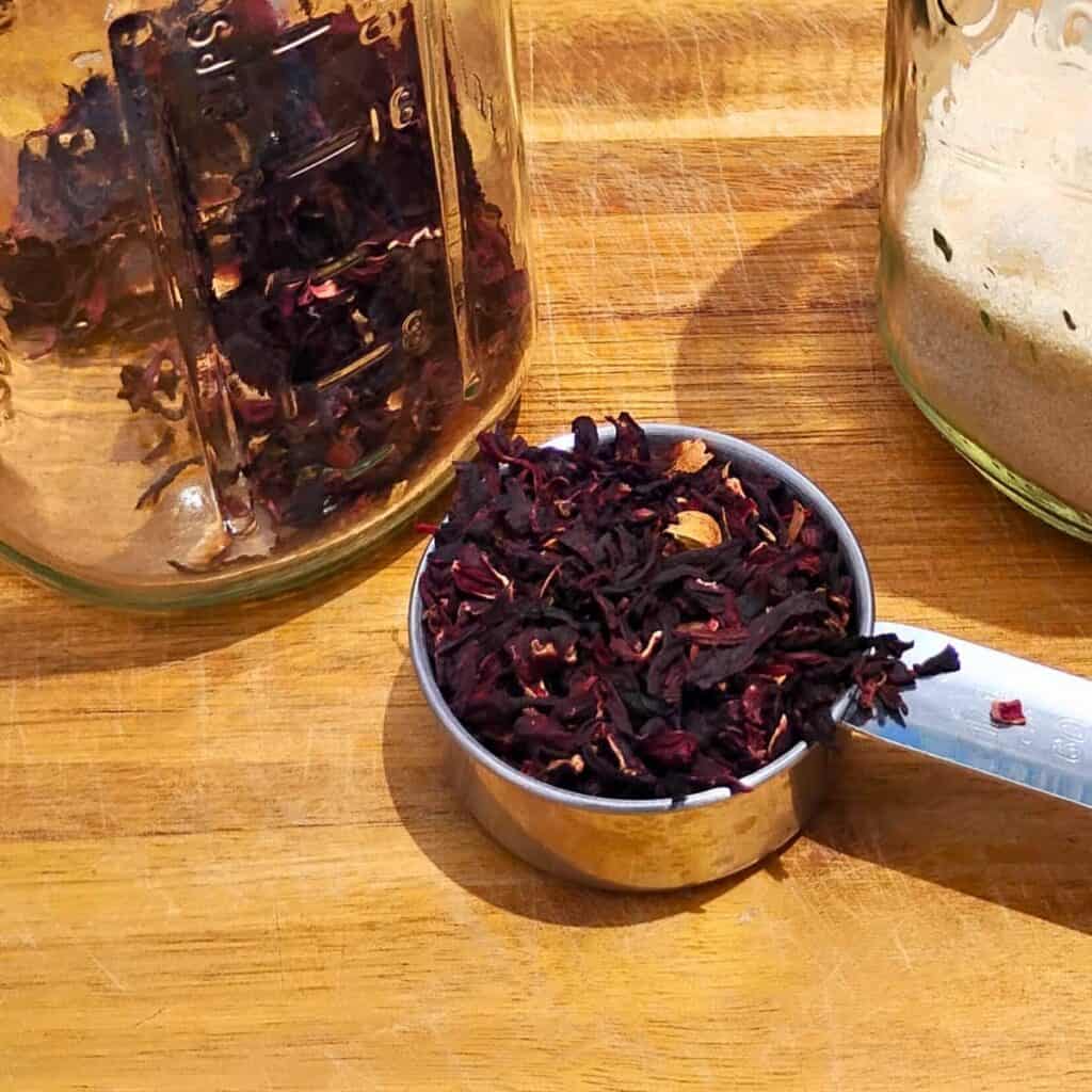 dried hibiscus calyxes in a measuring cup. There is a jar of hibiscus and one with sugar in the background.
