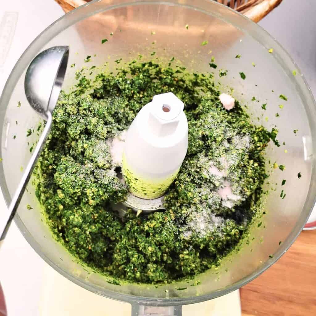 pesto getting salted in a food processor bowl.