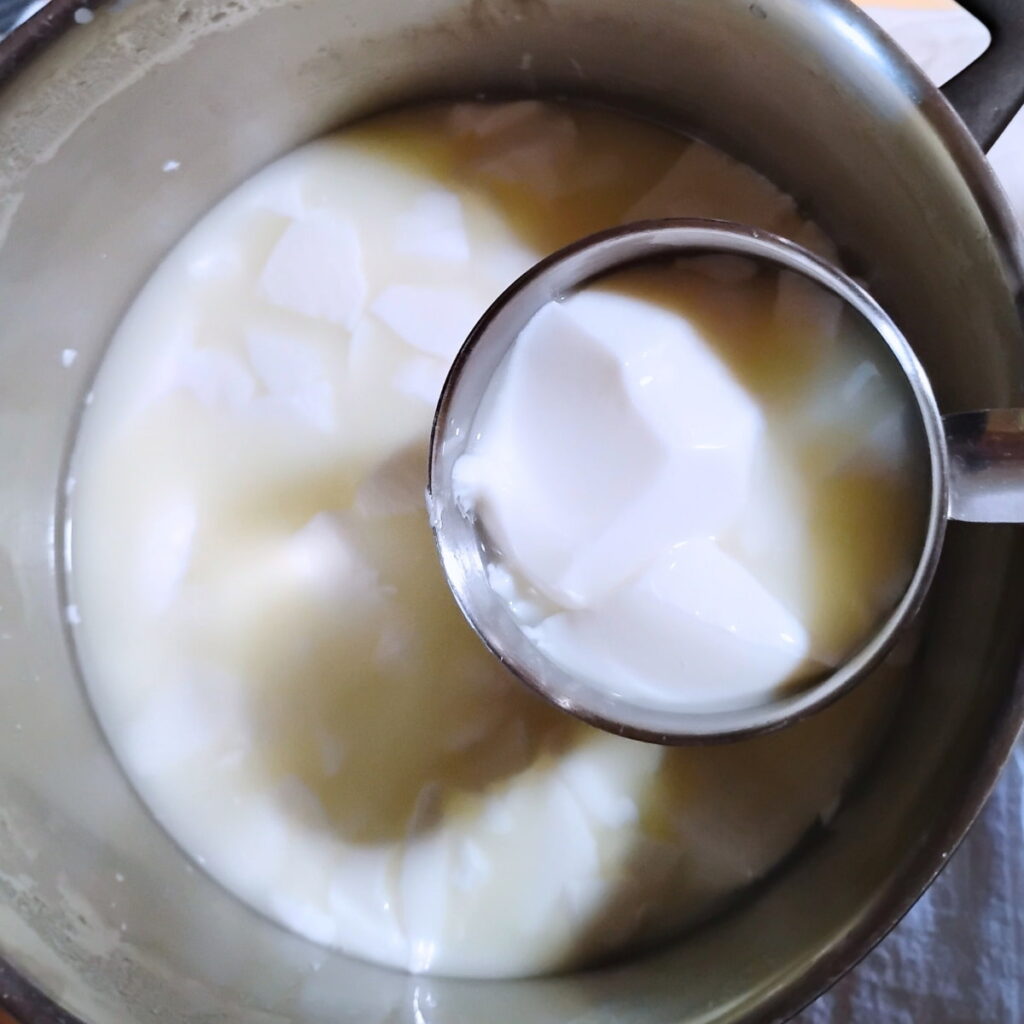cubes of cheese curd are gettin scooped out of a pot with a measuring cup.