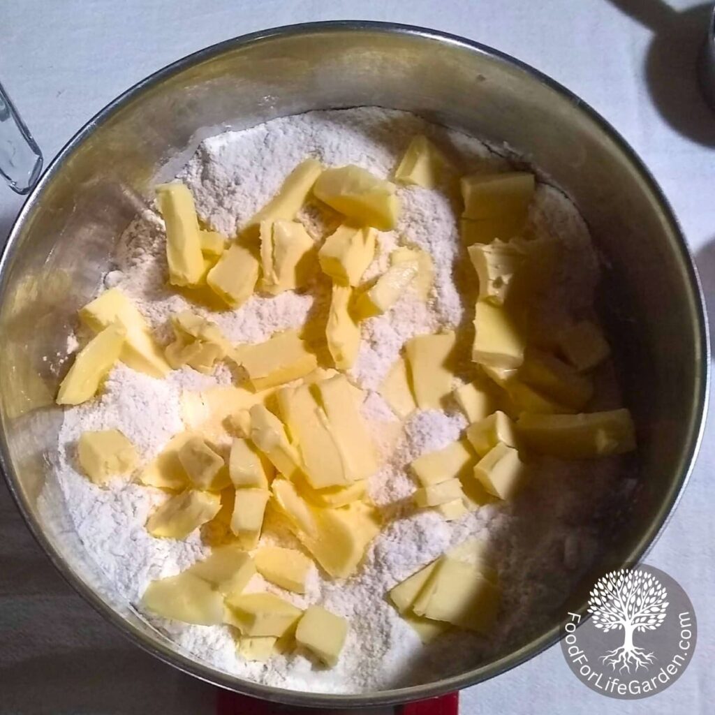 A bowl with shortbread crust ingredients and butter pieces scattered over it.