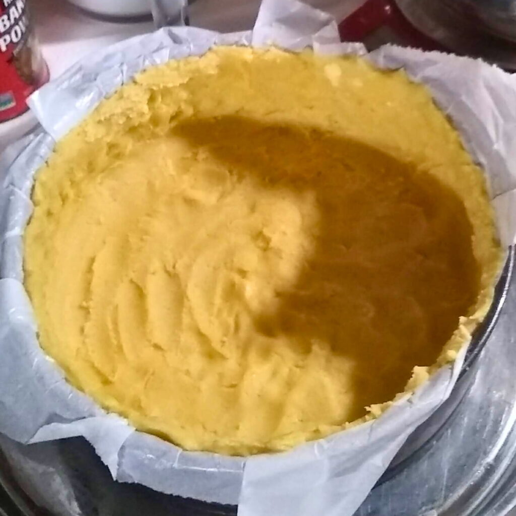 a cheese cake form with parchment paper and a shortbread crust that has been pushed into it.