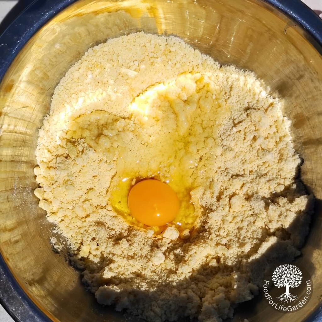 an egg is added to a crumbled mix of flour sugar and butter for making a cookie crust.