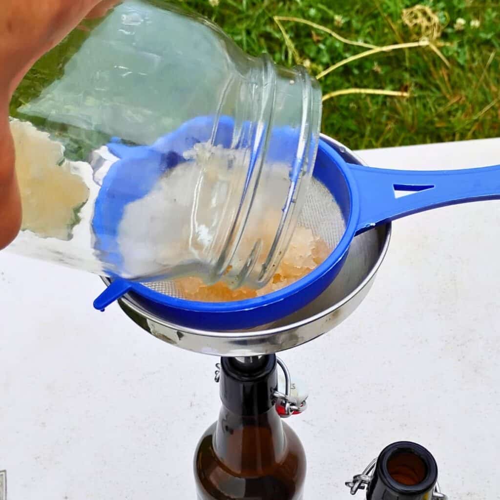 straining out waterkefir grains with a sieve and catching the liquid in the bottle via a funnel.