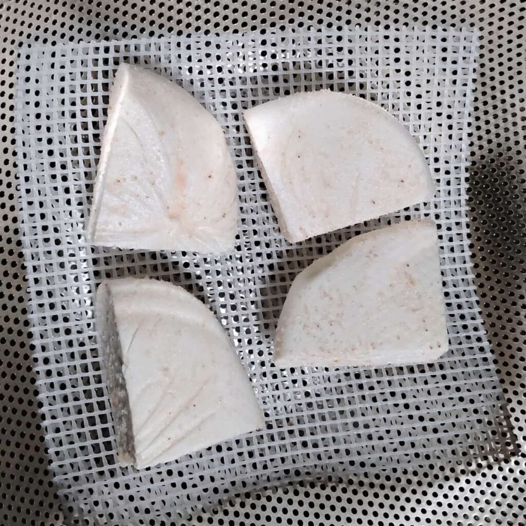 chunks of salted cheese on a drying mat in a colander.