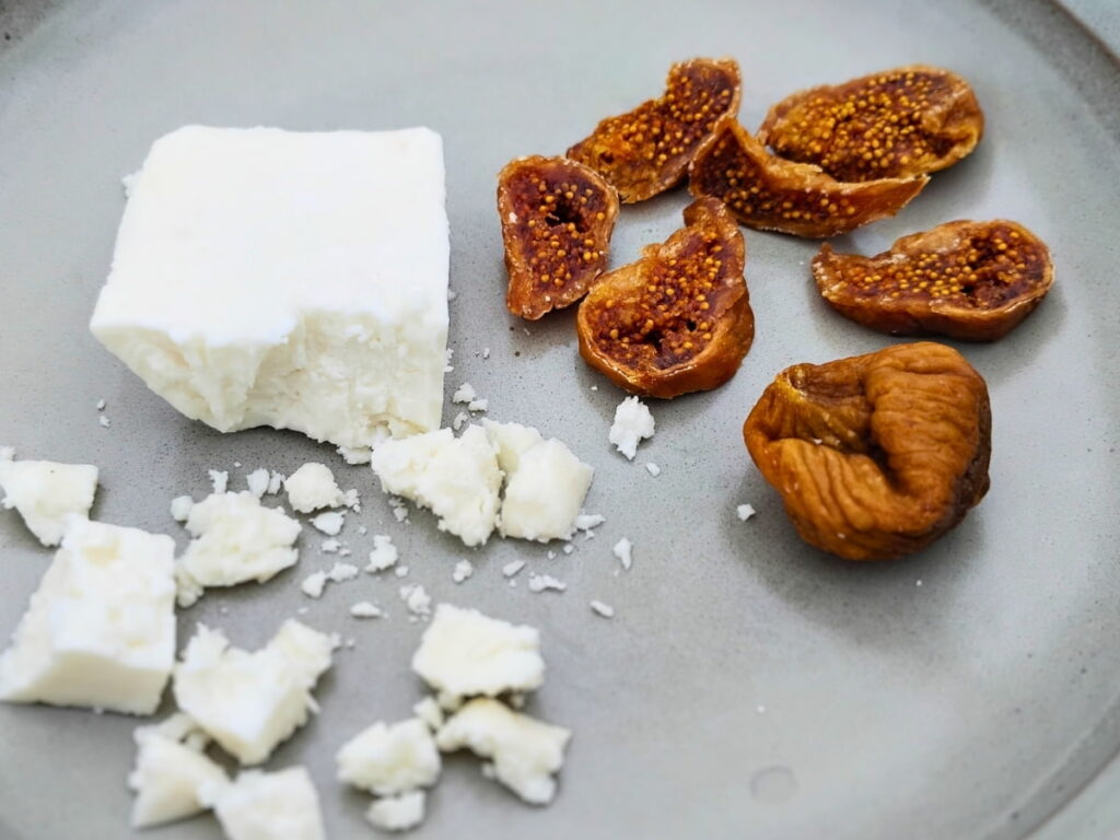 A plate with cut up dried figs and a chunk of bulgarian white cheese with some broken off pieces.