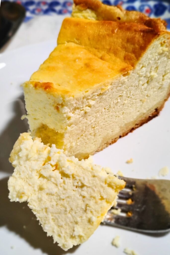 photo of a slice of German cheese cake or käsekuchen. there is a fork in the foreground that has a piece on it.