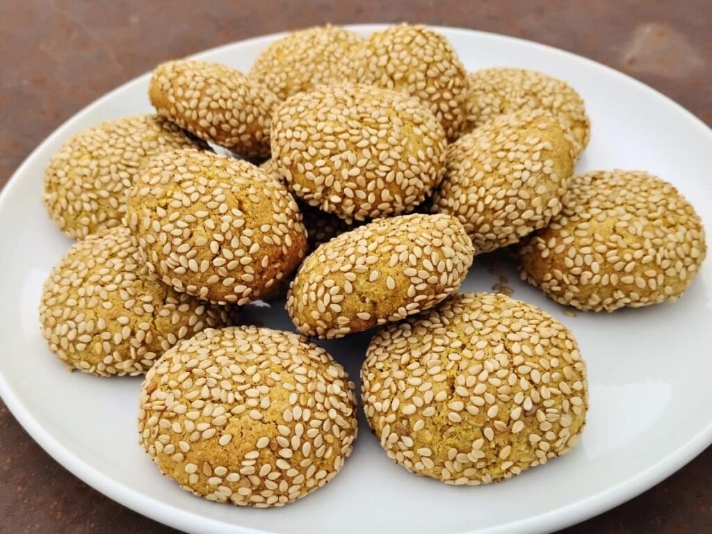 A plate full of honey lemon tahini cookies, coated with sesame seeds.