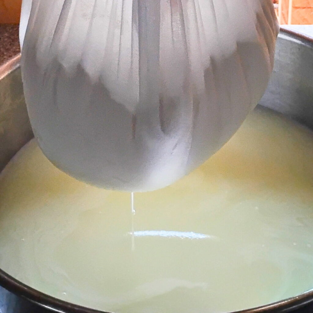 bulgarian white cheese dripping out of a bag into a bowl, that is catching a lot of whey