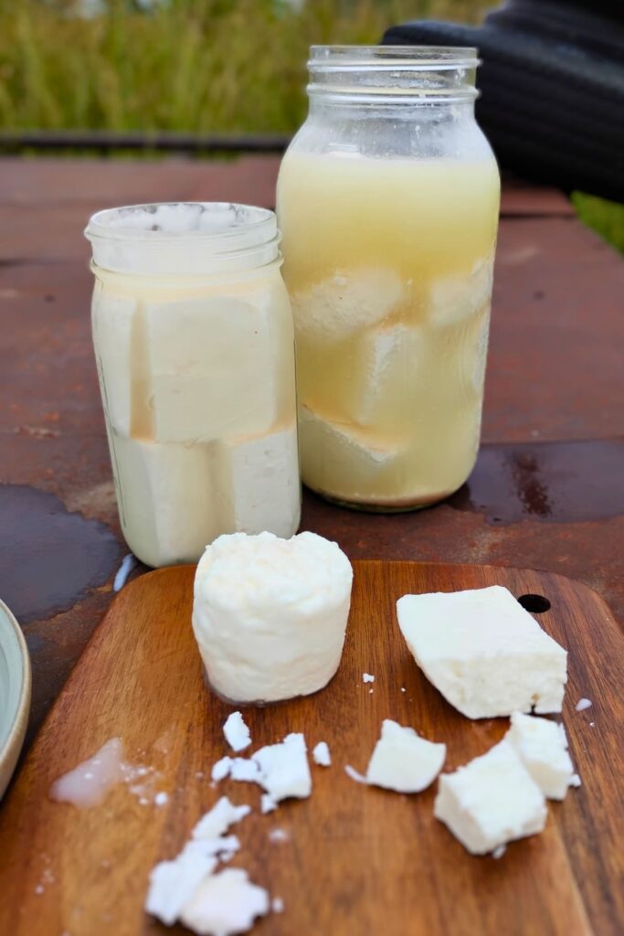 two large jars full of bulgarian feta cheese with a few chunks on a cutting board in the foreground.