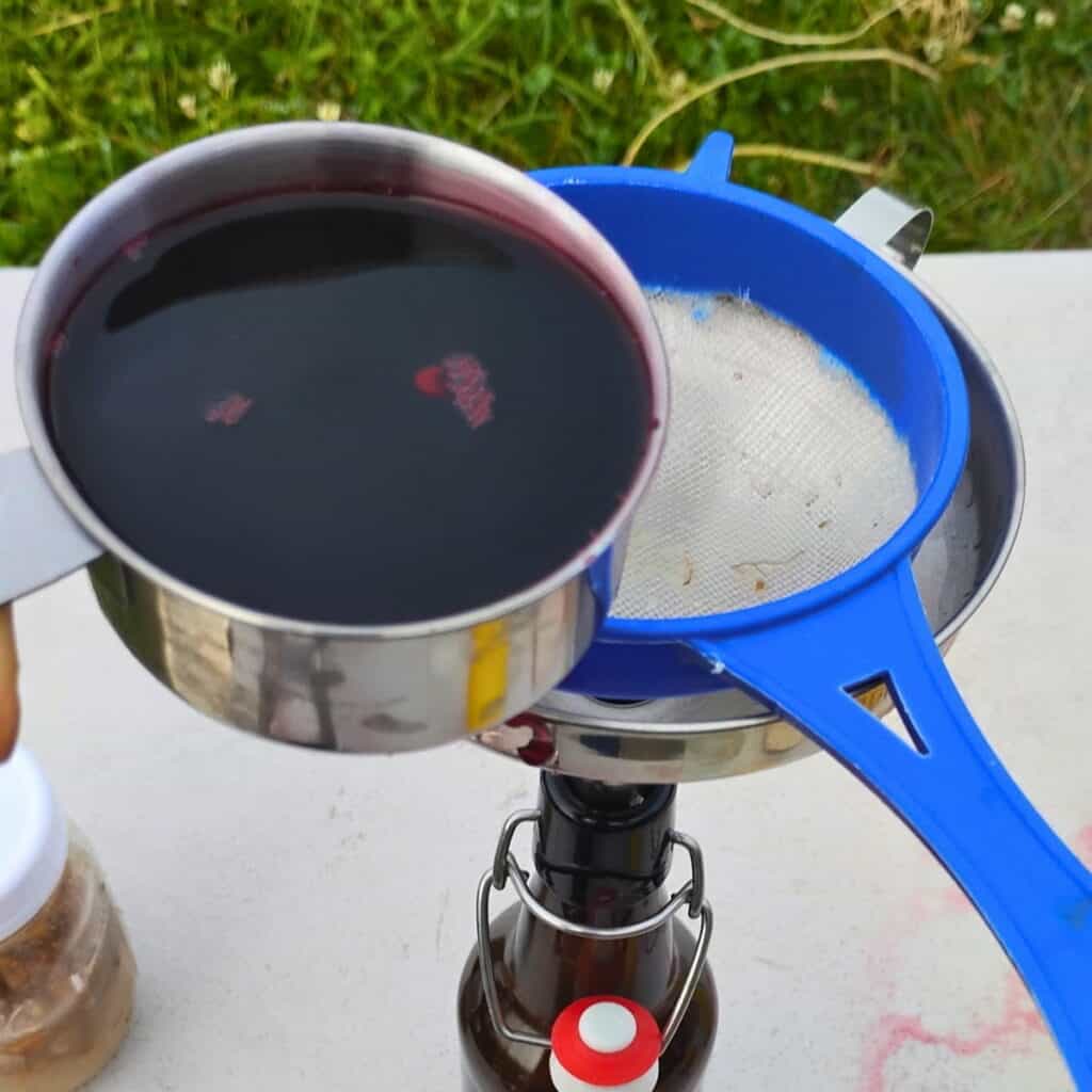 adding hibiscus syrup to the bottle via a strainer and funnel.