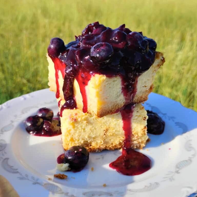 two pieces of cheesecake stacked on top of each other with lemon blueberry sauce poured over them, on a plate.