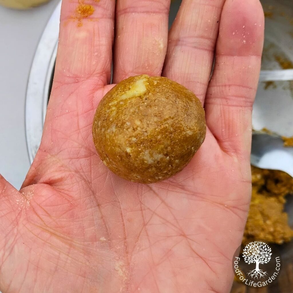 A hand holding a rolled up ball of honey tahini cookie dough ready to roll in sesame seeds.