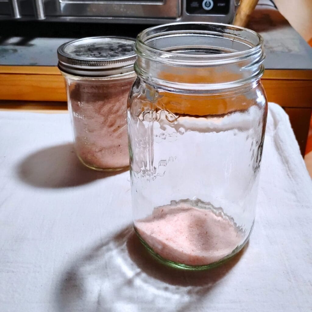 Jar of salt in the background and a quart jar with a quarter cup of salt in front of it.