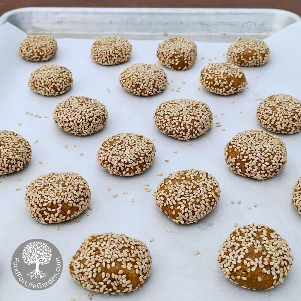 lemon tahini spice cookies, rolled in sesame seeds on a baking sheet and flattened ready for the oven.