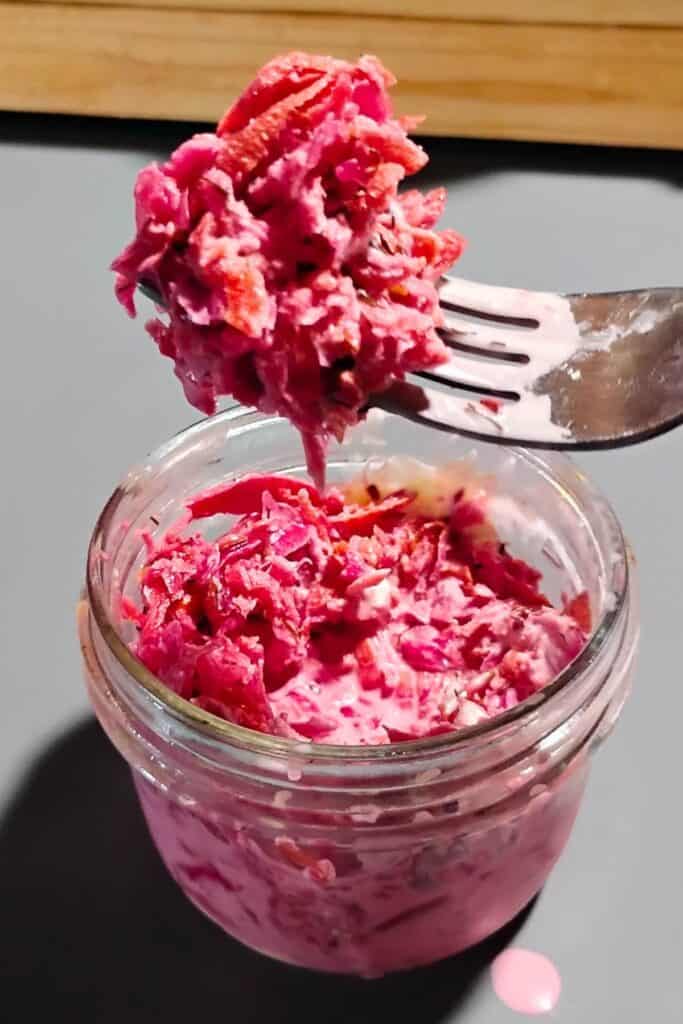 photo shows fermented coleslaw in a small bowl, mixed with mayonnaise. a fork is removing a portion of it.