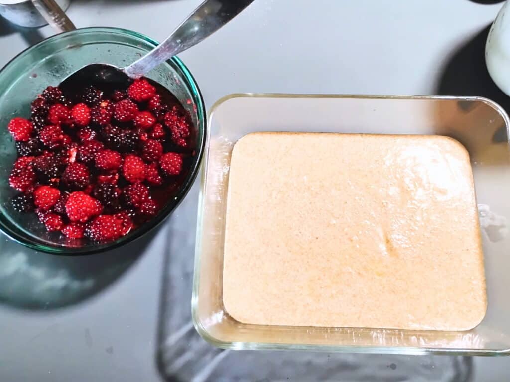a pan with batter across the bottom and a bowl of blackberries beside it. 