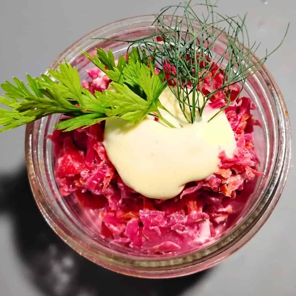 small bowl filled with fermented garden slaw and topped with homemade mayonnaise and some herbs.