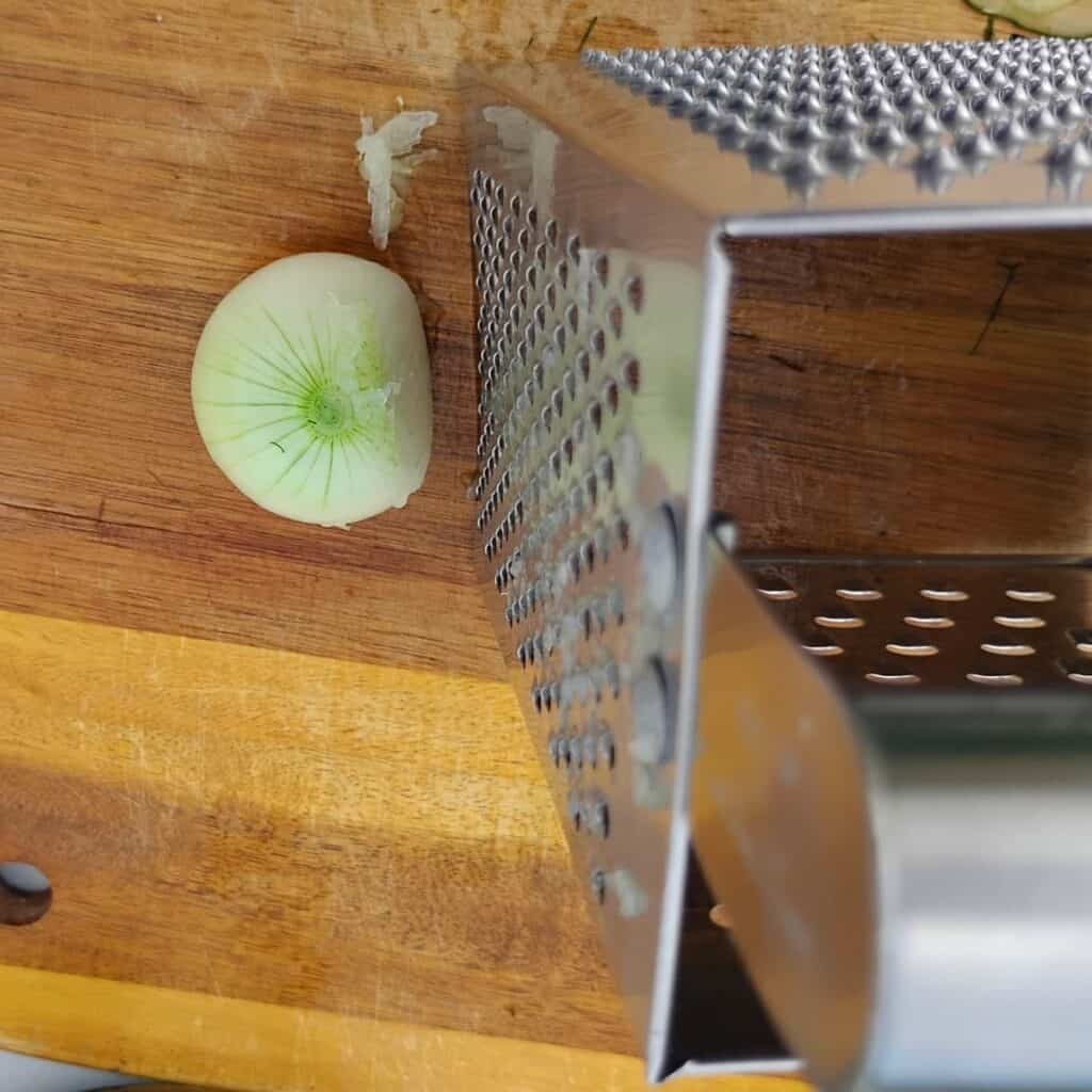 An onion is getting finely grated on a cheese grater.