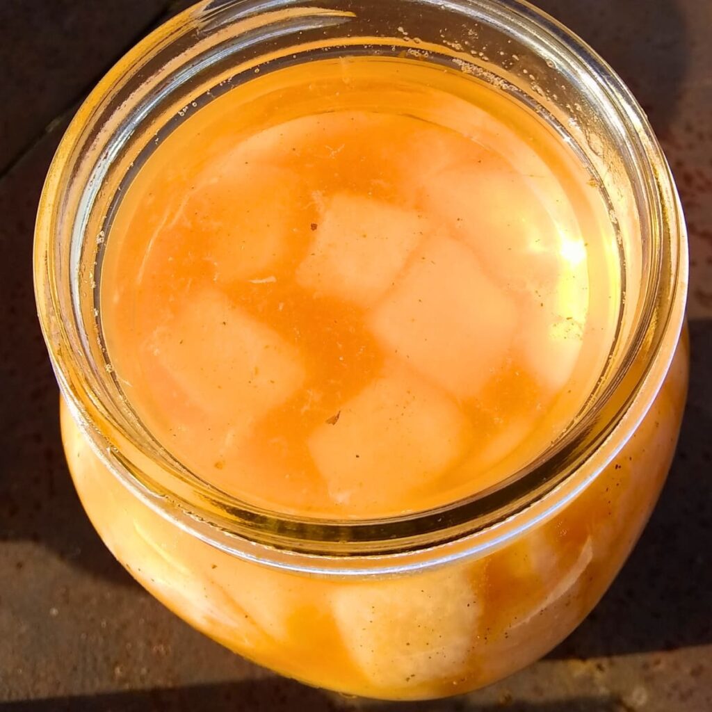 top view of a jar full of fermented cantaloupe pieces with a glass fermentation weight on top. 