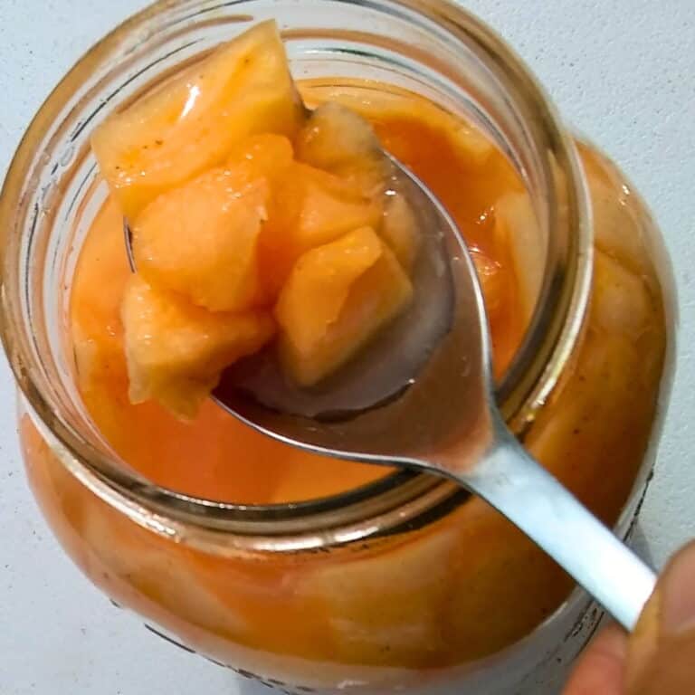 fermented cantaloupe pieces on a spoon, taken from a jar below.