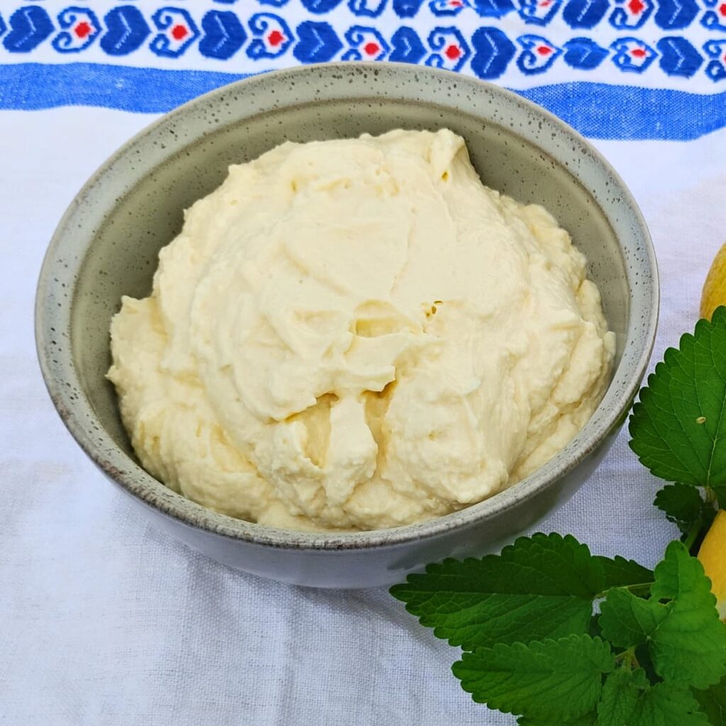 photo shows a bowl filled with lemon cheesecake mousse on a cloth and with lemon balm and lemons beside it.