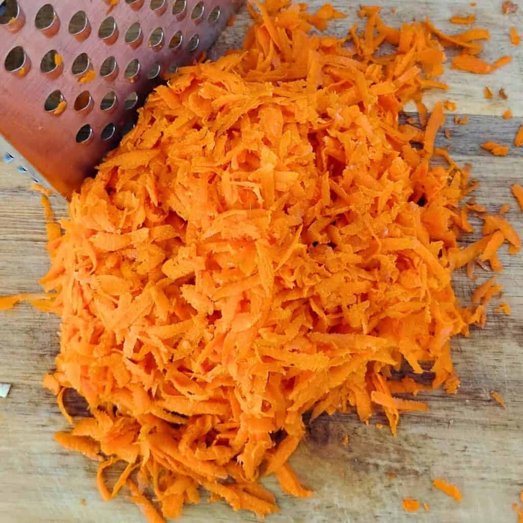 grated carrot and a grater on a cutting board.