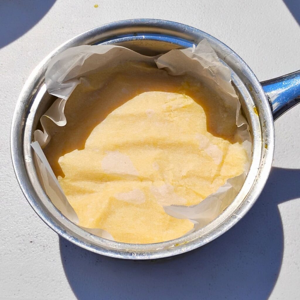 A small pot with lemon curd and a parchment paper covering it to prevent a skin from forming