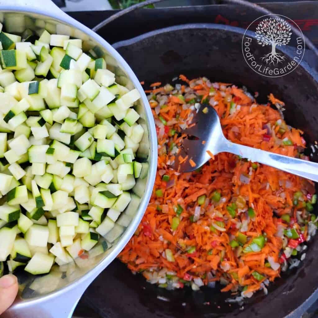 chopped zucchini are added to a dutch oven with other vegetables in it.