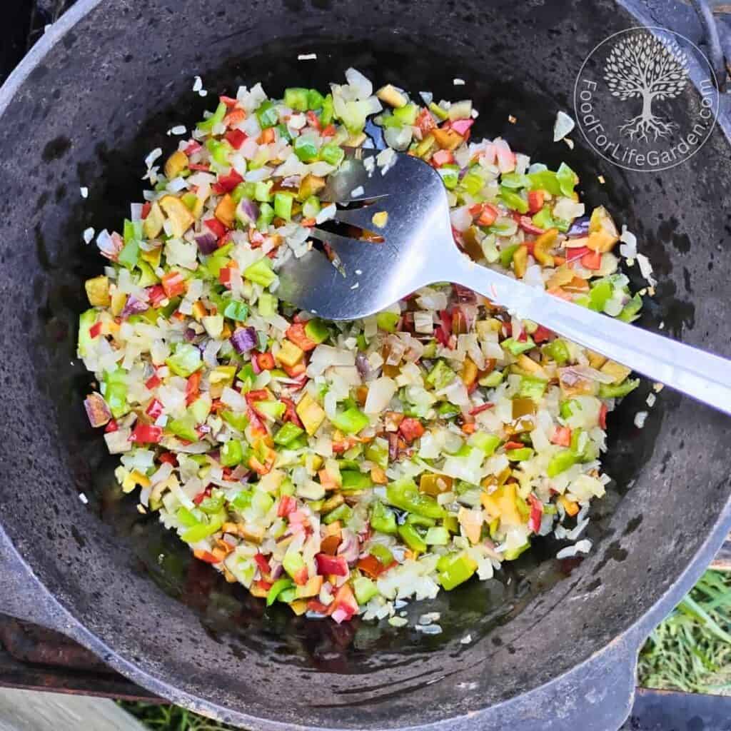 a dutch oven with mixed peppers, garlic, and onions in oil.